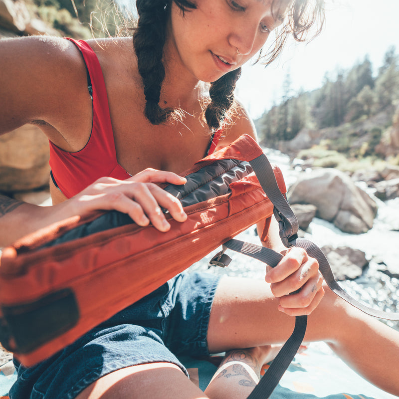 Load image into Gallery viewer, Woman sitting in a forest rolling up her crazy creek chair in copper