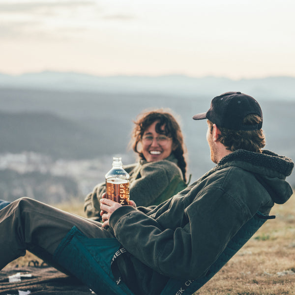 Two people laughing and talking sitting in chairs on the top of a mountain at sunset