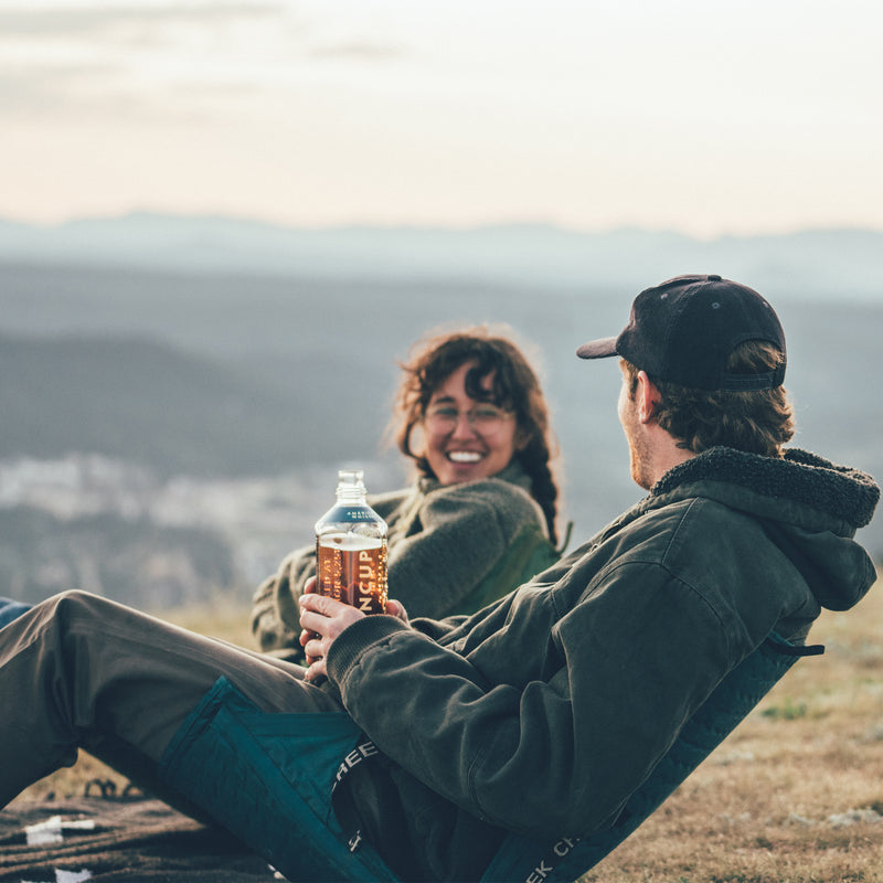 Load image into Gallery viewer, Two people laughing and talking sitting in chairs on the top of a mountain at sunset
