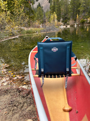 Blue Canoe IV crazy creek chair strapped to a red canoe next to a river