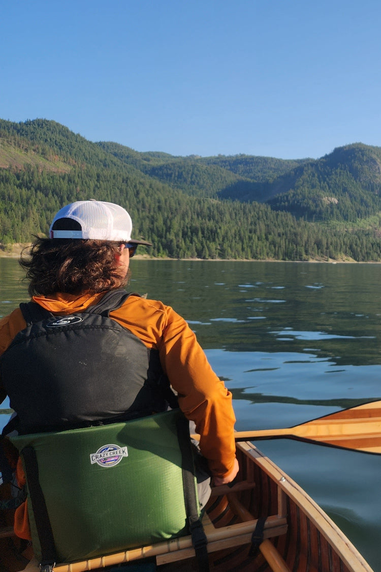 Man sitting on a canoe using a Crazy Creek Canoe Chair III, enjoying comfort and support while paddling.