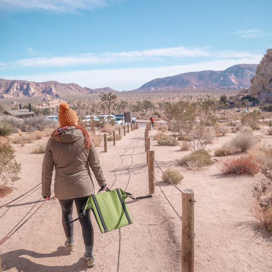 Woman carrying a green Crazy Creek The Chair through a mountainous Western US desert landscape.