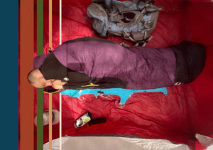 Person lying on a red sleeping bag and unfolded Crazy Creek Air Lounger sleeping pad with camping gear around