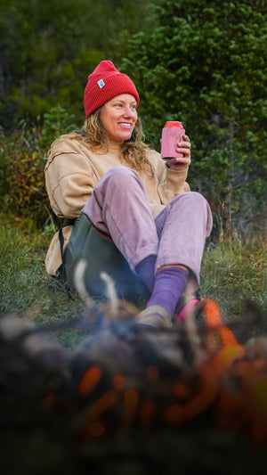 Woman holding a drink sitting in a crazy creek chair in front of a bonfire