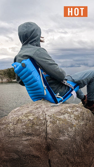 Person sitting in an inflatable blue chair on a pointy rock overlooking a lake