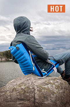 Person sitting in an inflatable blue chair on a pointy rock overlooking a lake
