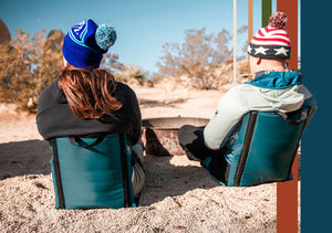 A couple sitting in crazy creek chairs next to a fire ring in the desert