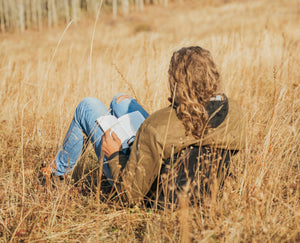 Person reading a book while sitting in a Crazy Creek chair in a field