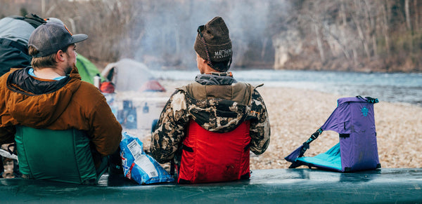 Two people sitting near a river while they sit in foldable crazy creek camping chairs