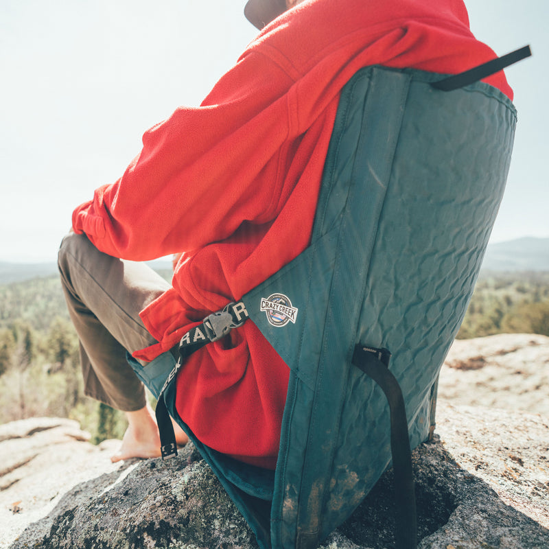 Load image into Gallery viewer, Person sitting on a rock wearing a red jacket sitting in a green crazy creek camping chair
