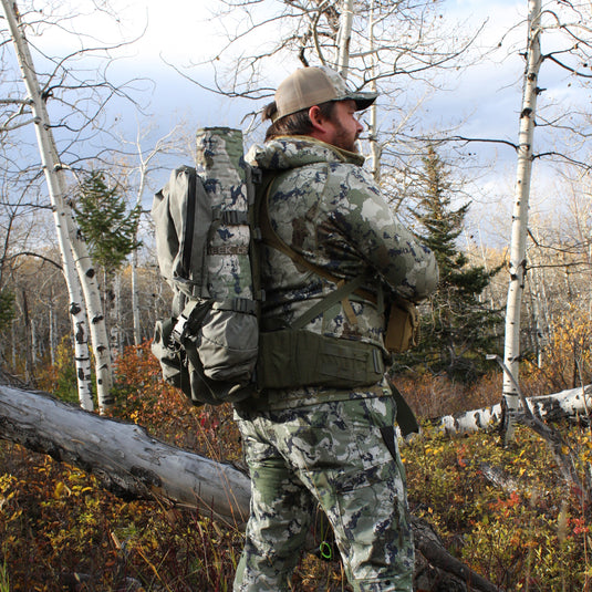 Man wearing a backpack with the crazy creek rolled up and attached to the side of it. 