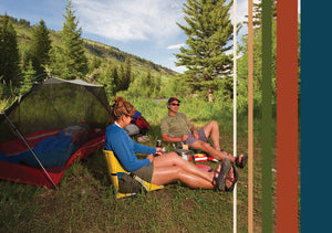 A couple sitting in their crazy creek chairs in front of their tent in the woods making dinner