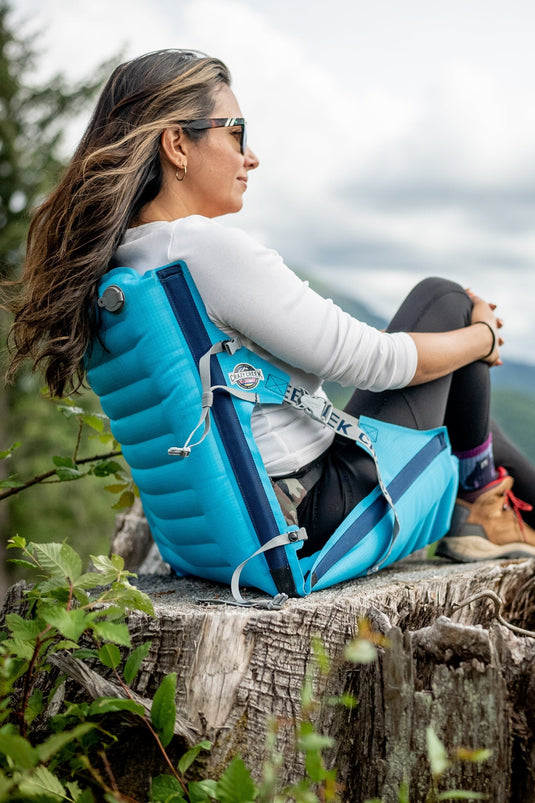 Woman relaxing outdoors on a Crazy Creek AirCliner, enjoying lightweight and portable comfort.