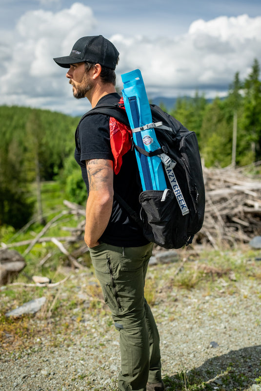 Man hiking on a trail with a Crazy Creek AirCliner rolled up and tucked into the side pocket of his backpack.