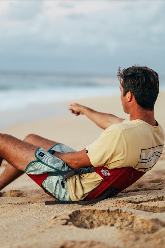 Man sitting on a beach using a Crazy Creek HEX 2.0 LongBack Chair in Red, enjoying the coastal view.