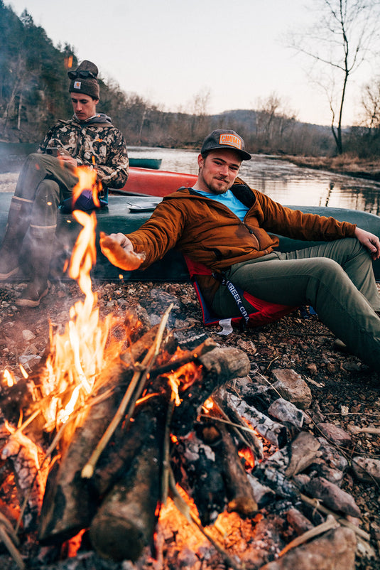 Person relaxing in a Crazy Creek Original Chair by a campfire.